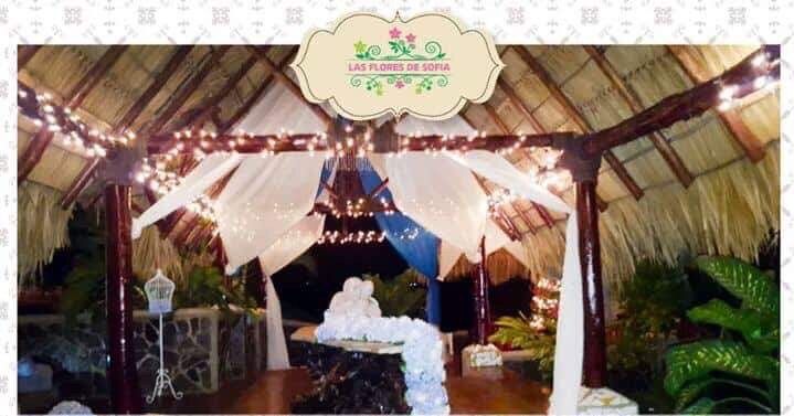 Tropical wedding canopy with white drapes, string lights, and a decorated table at night