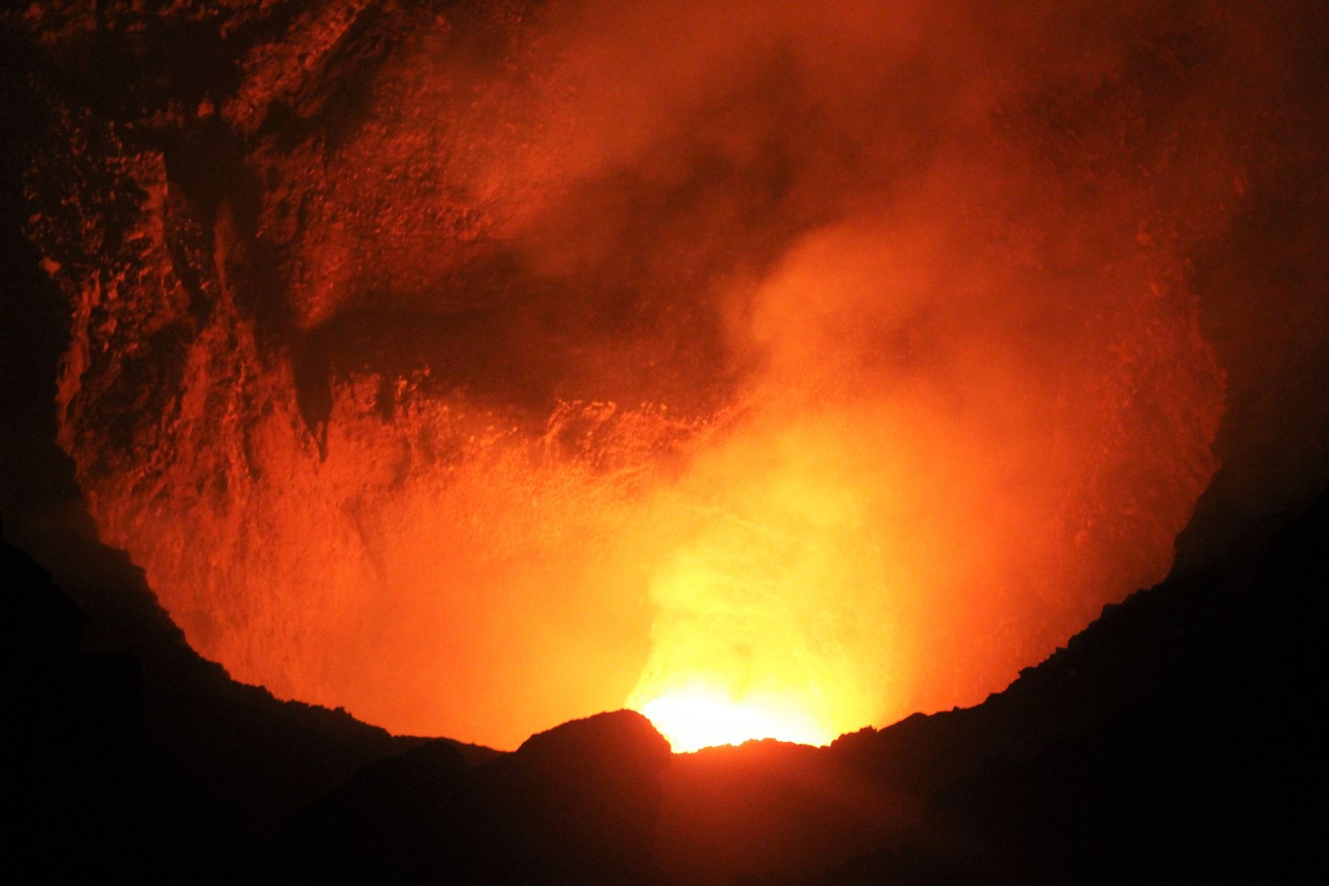 Glowing orange lava or fire beneath a dark rocky opening, like a volcano or cave at night