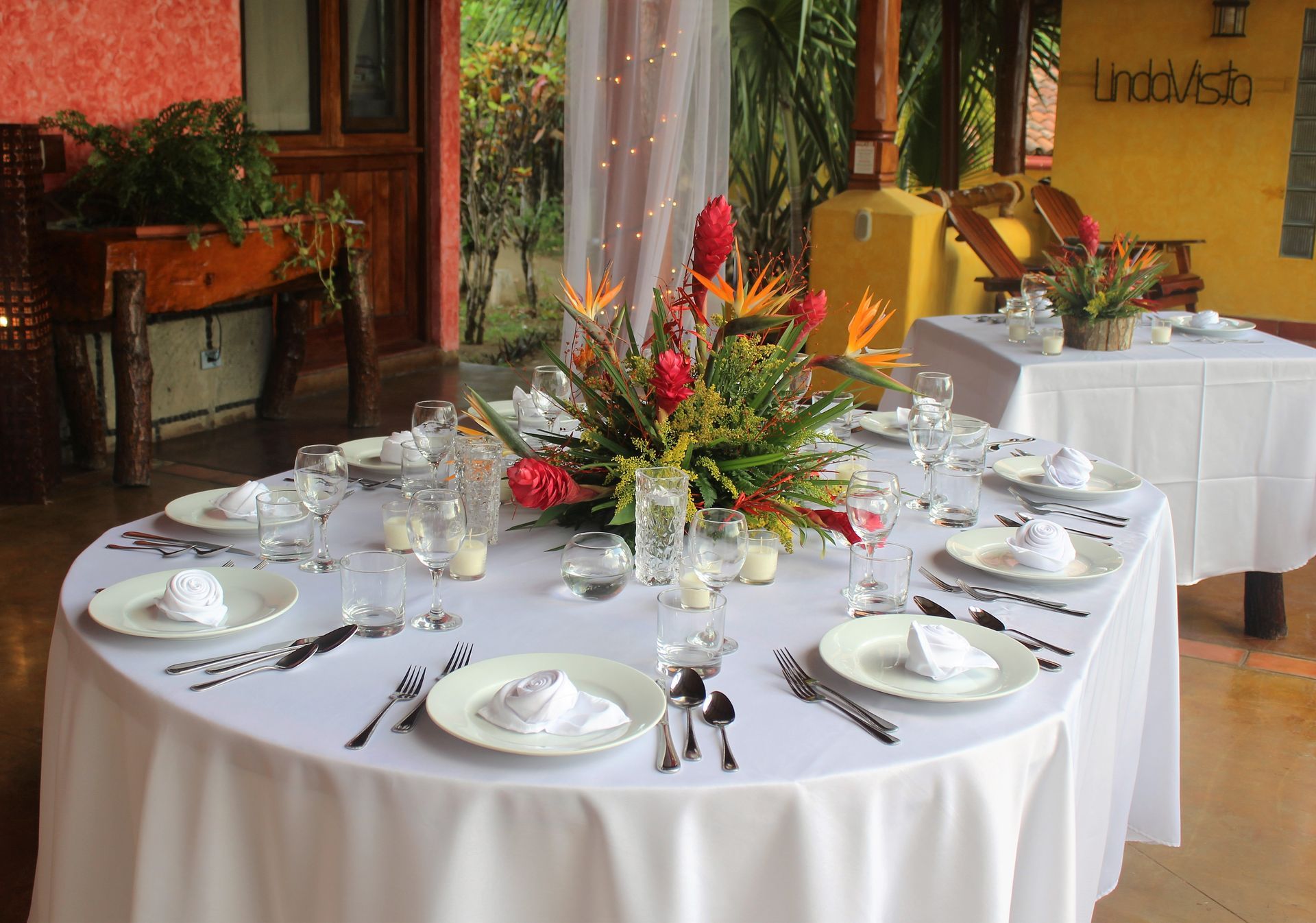Round banquet table with white linens, floral centerpiece, and place settings in a patio dining area