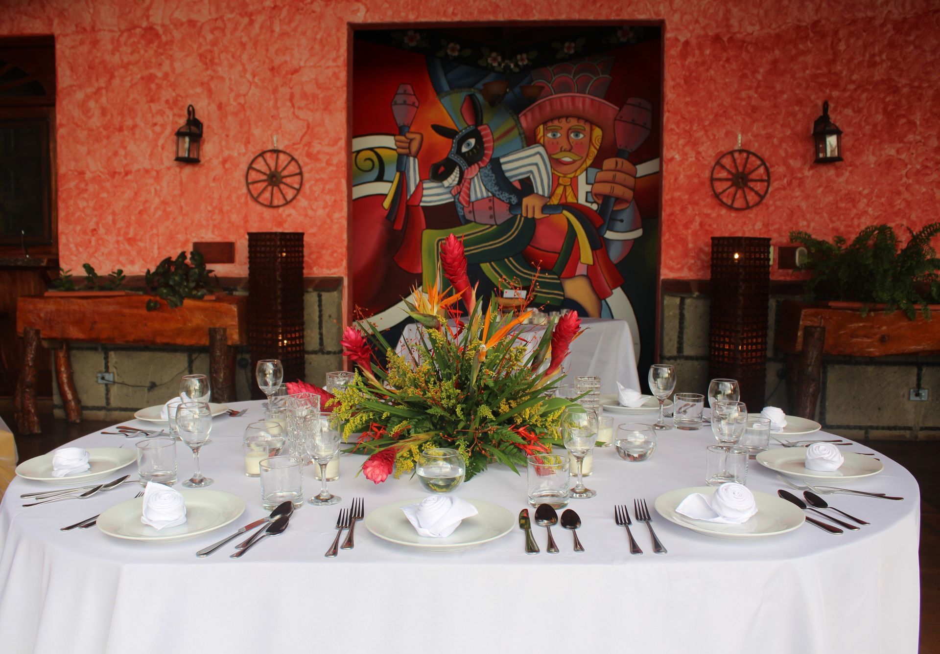 Elegant dining table set for a formal event, with white linens, floral centerpiece, and colorful mural backdrop.