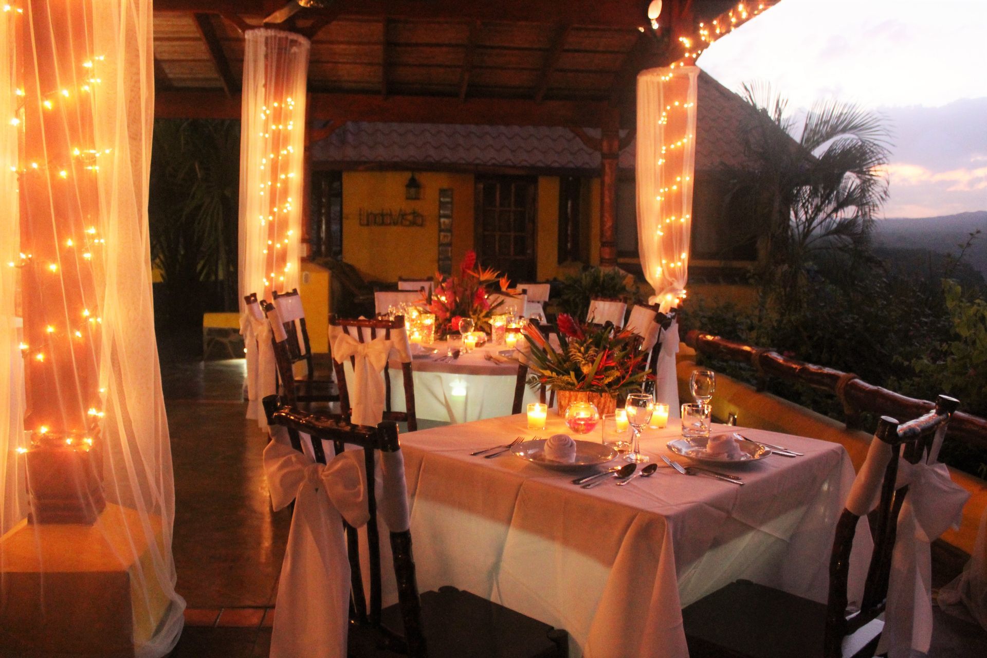 Romantic outdoor restaurant terrace at sunset, with candlelit tables and fairy lights overlooking a scenic view