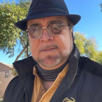 Man in a black hat and glasses outdoors under a bright blue sky