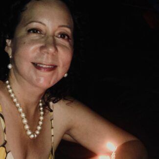 Smiling woman in a pearl necklace lit by candlelight in a dark setting