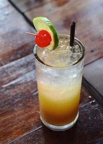 Tall tropical cocktail with a lime slice, cherry, and straw on a wooden table.