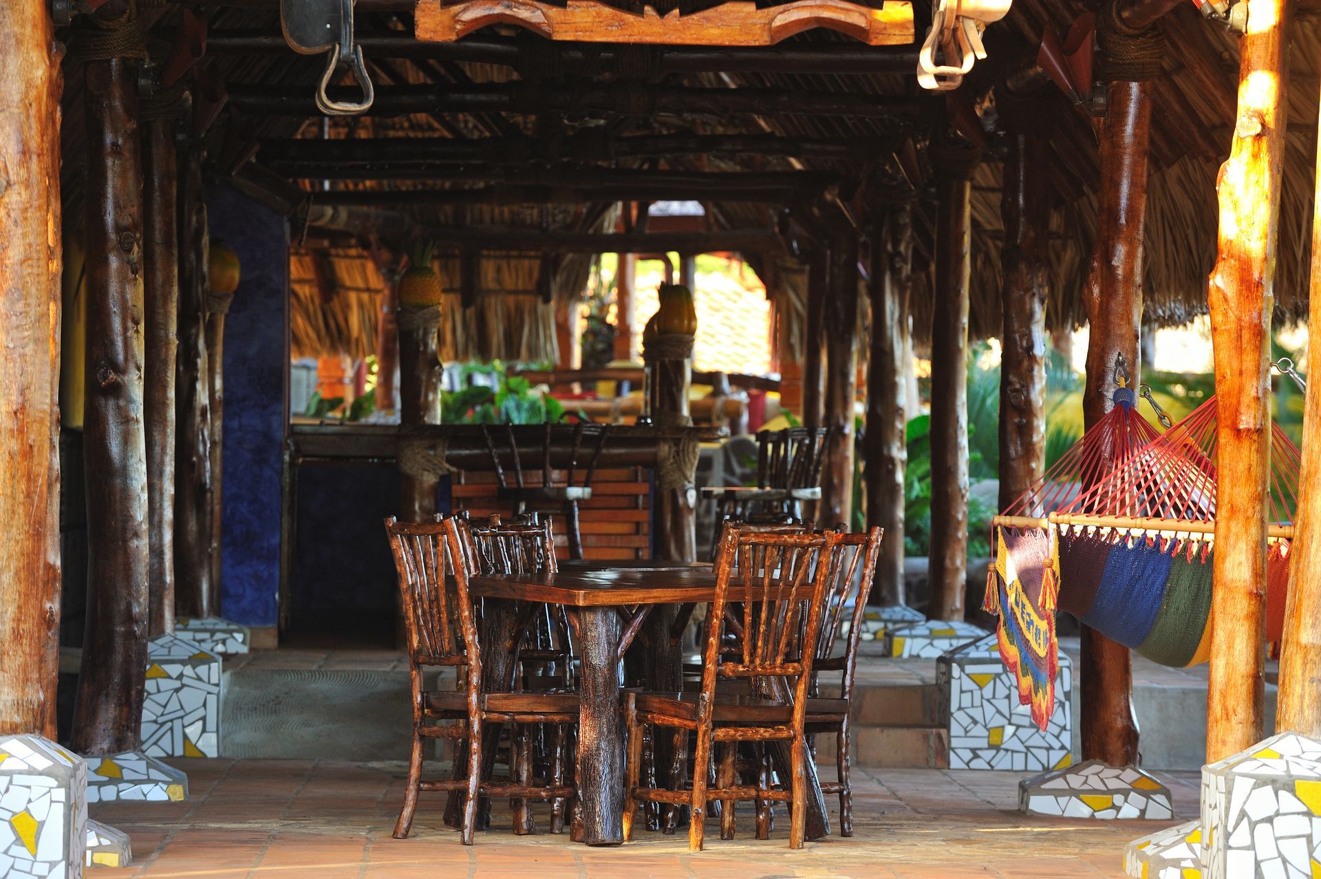 Rustic open-air restaurant with wooden tables and chairs under a thatched roof