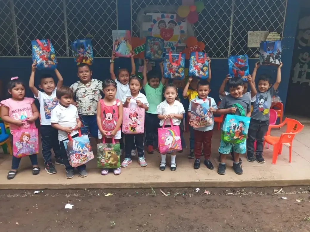 Children posing with colorful gift bags in front of a decorated wall at a school or community event