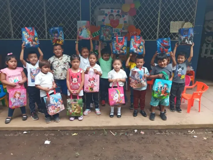 Children posing with colorful gift bags in front of a decorated wall at a school or community event