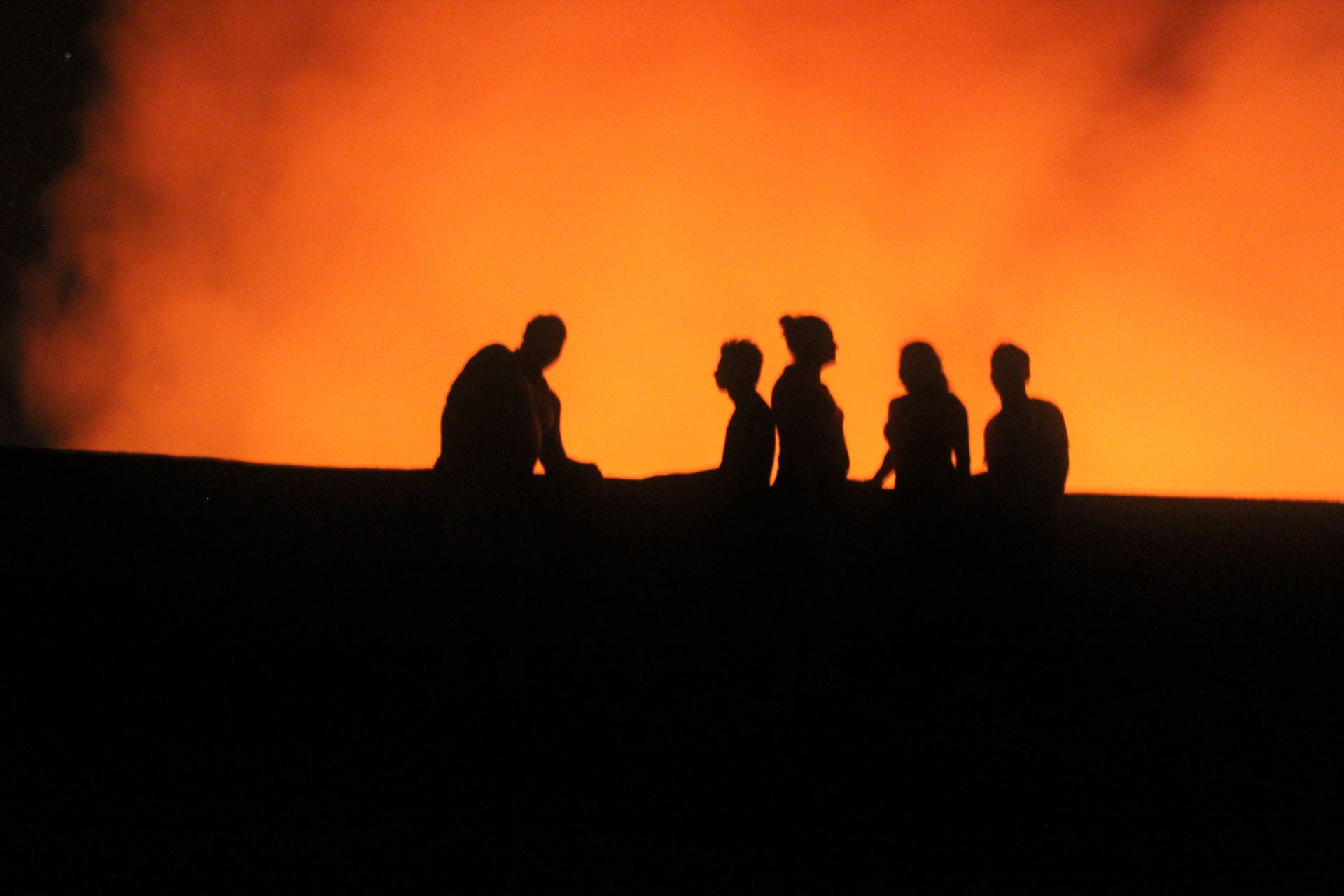 Silhouetted people standing against a bright orange sunset sky
