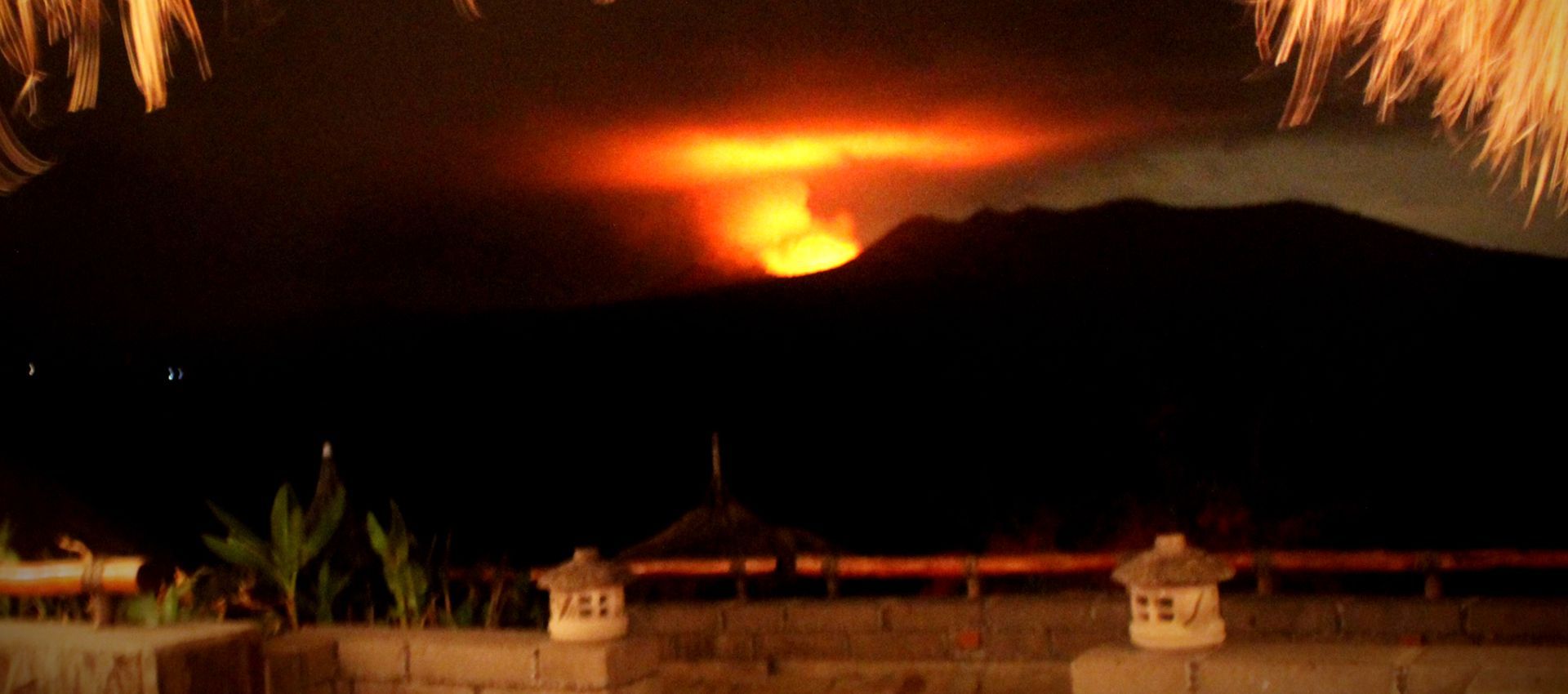 Volcano erupting at night behind a dark mountain silhouette, glowing orange lava and smoke
