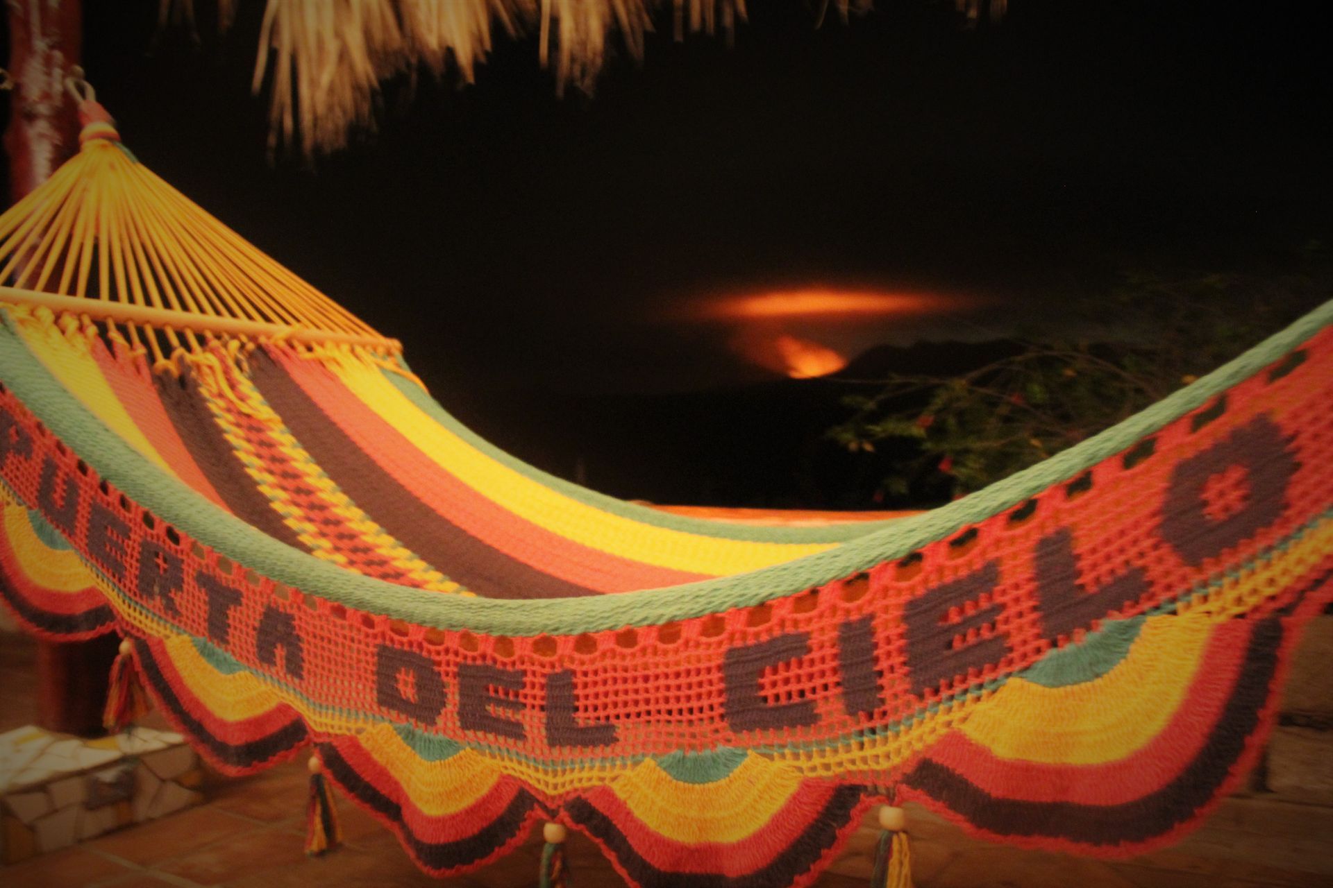 Colorful striped hammock with “CARTA DEL CHI…” text at night on a beach, with a distant firelight
