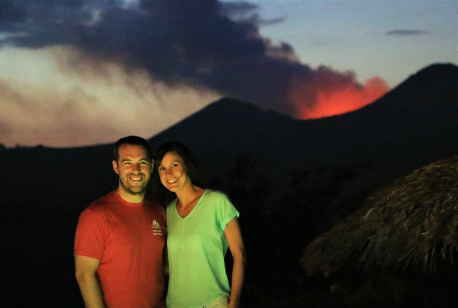 Two people smiling at dusk with a glowing volcano in the background