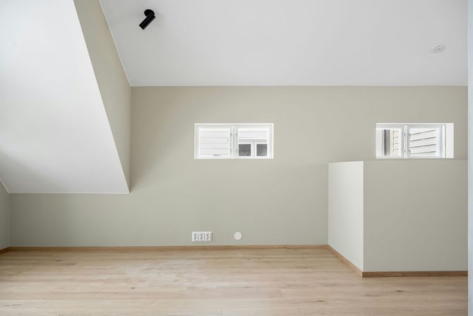Empty modern room with light wood floors, pale walls, and small windows.