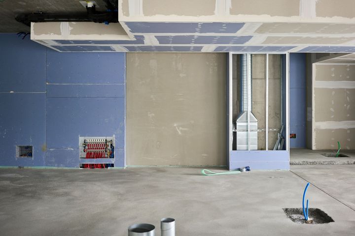 Unfinished interior with blue and beige walls, exposed ceiling, and a central metal duct in a construction site.