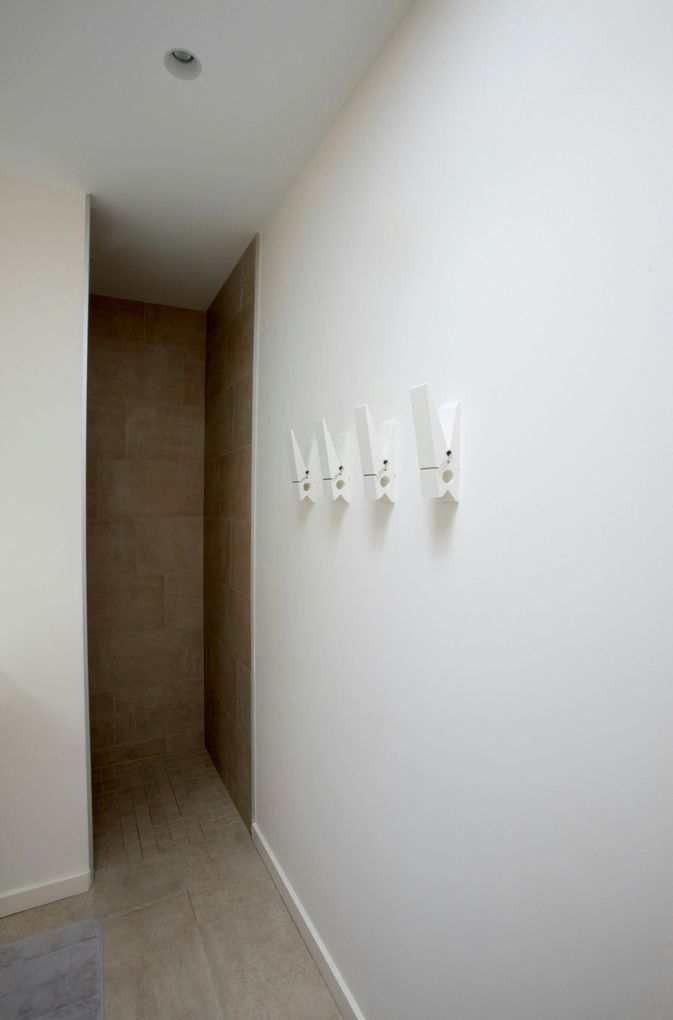Narrow hallway with white walls, beige floor, and wall-mounted hooks on the right.