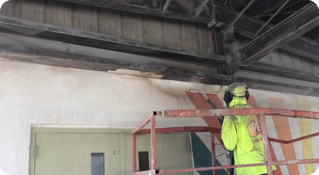 Worker in neon jacket standing on a red scaffold, inspecting the ceiling in an industrial room.