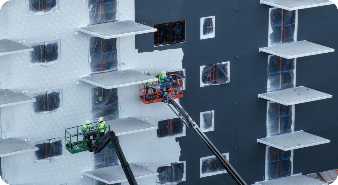 Two drones inspect a snowy apartment building facade, one green and one orange, near balconies and windows.