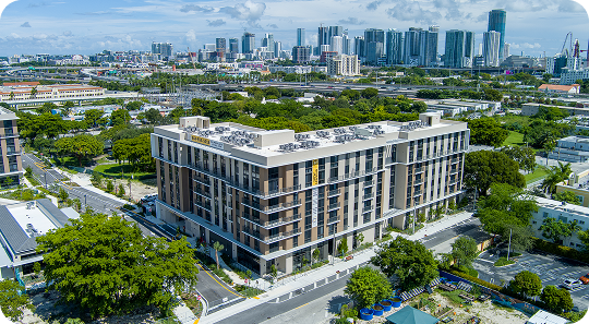 Aerial view of a modern office building with a city skyline and trees in the background.
