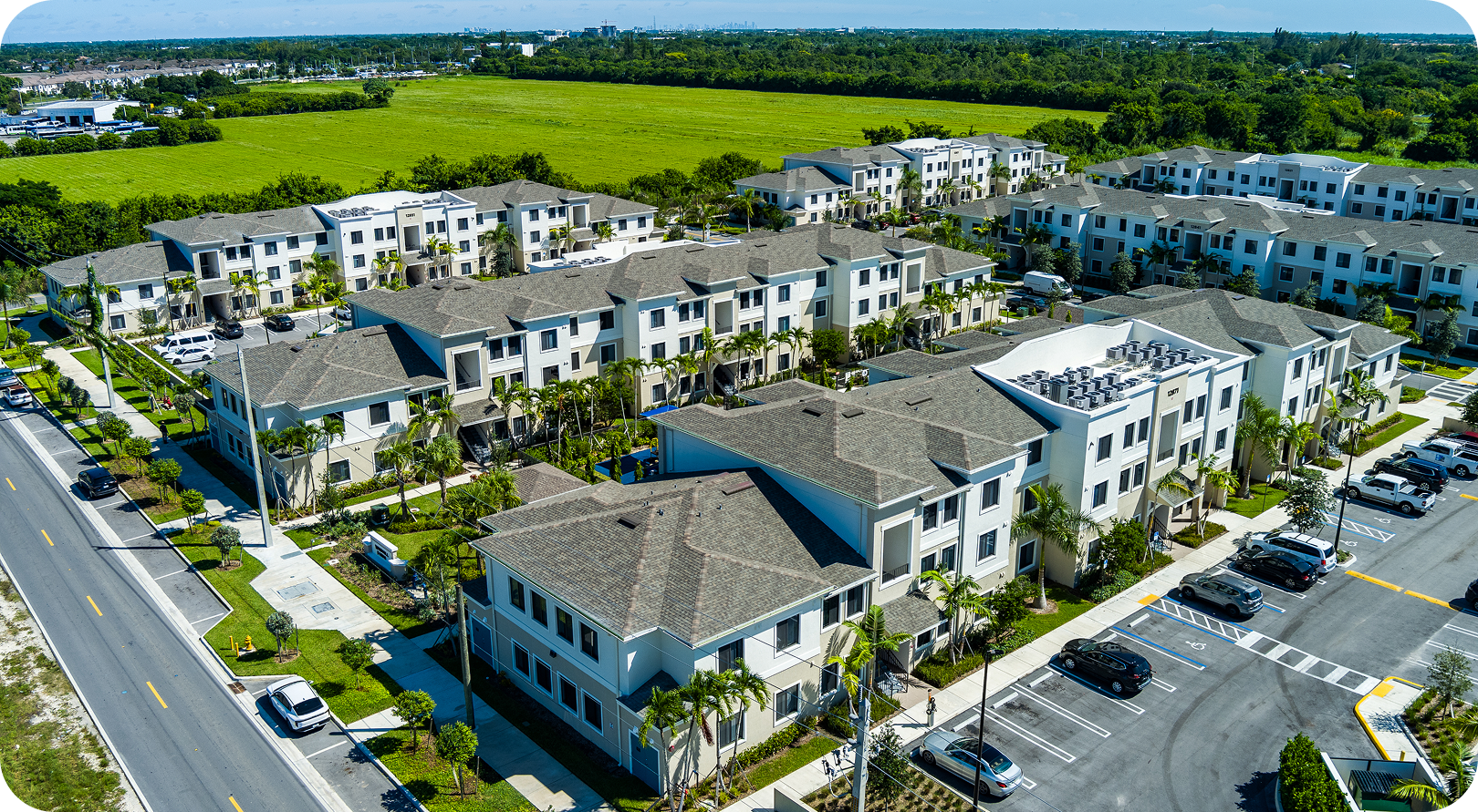 Aerial view of a modern apartment complex with white buildings, parking lots, and green landscaping