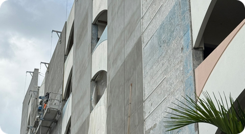 Gray concrete apartment building with curved balconies and palm leaves in the foreground