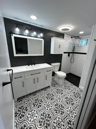 Modern black-and-white bathroom with patterned tile floor, white vanity, toilet, shower, and mirror lights