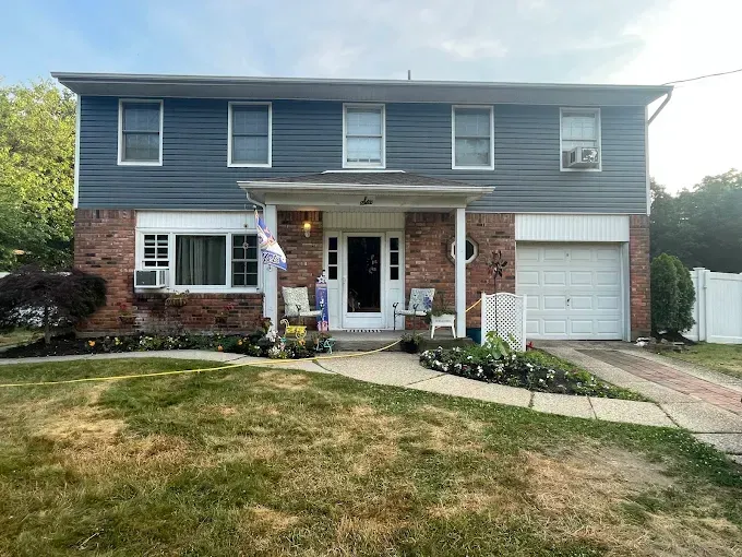 Two-story brick and blue house with front porch, garage, and sloped front yard