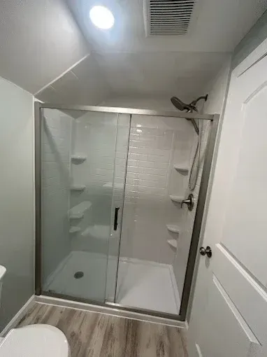 Modern bathroom with glass shower enclosure, white tile, and wood-look flooring