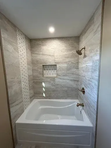 Modern tiled bathroom with a white soaking tub, shower fixtures, and recessed wall niche
