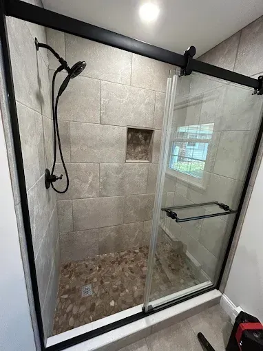 Modern shower stall with glass door, rainfall showerhead, tiled walls, and pebble shower floor.