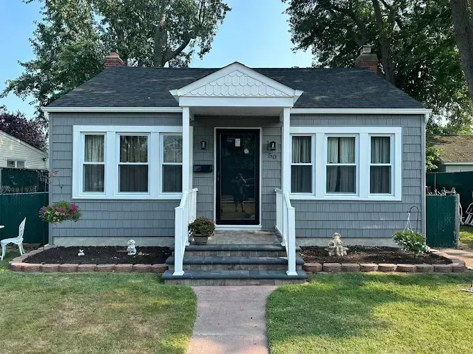 Small gray cottage with white trim, front steps, and a central porch door in a grassy yard