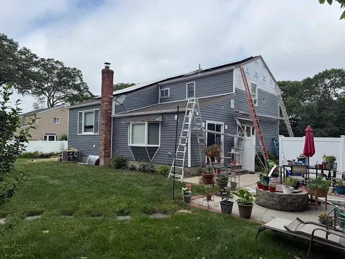A gray house with ladders and potted plants in the yard, suggesting exterior maintenance or renovation.