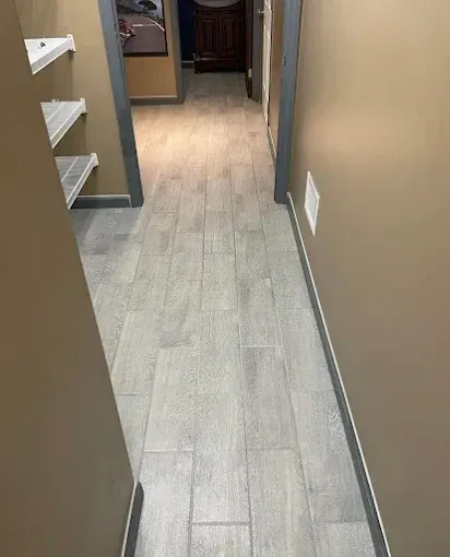 Narrow hallway with beige walls, light wood flooring, and white shelves on the left