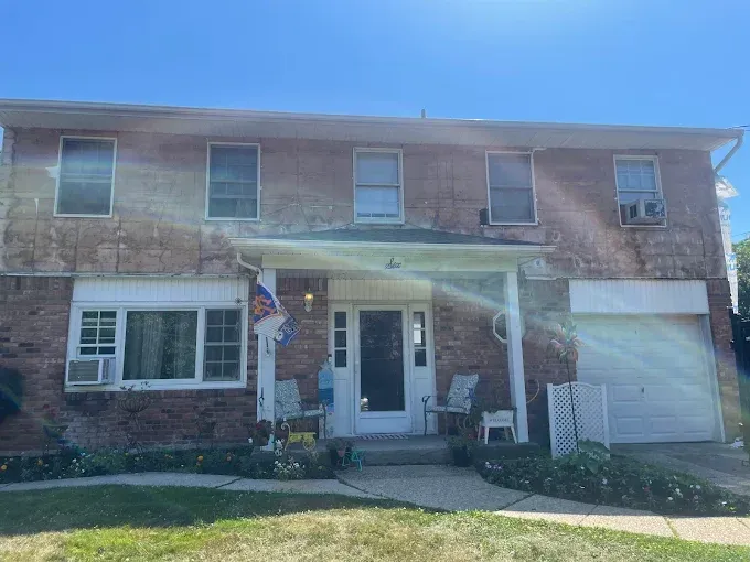 Two-story brick house with a front porch, garage, and bright sun glare in front.