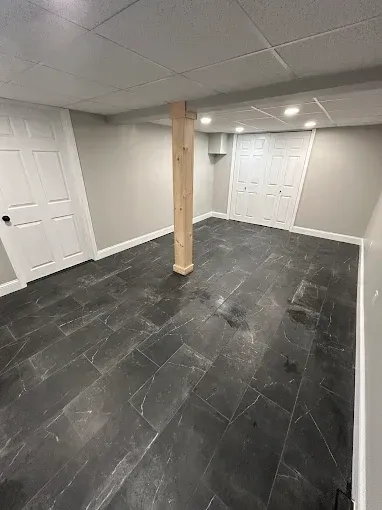 Empty basement room with white doors, gray tile floor, and a central wooden support post.