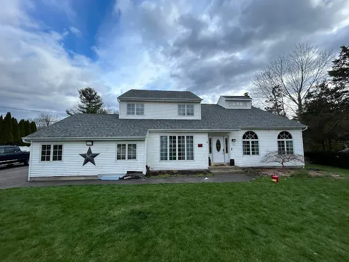 White two-story house with a green lawn and cloudy sky, featuring black shutters and a star decoration