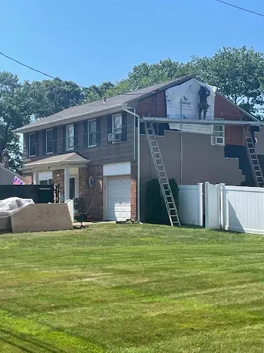 Two-story house with a ladder leaned against the roof during exterior repairs under a clear blue sky