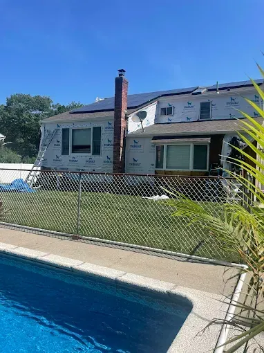 Backyard pool beside a house with a chain-link fence and blue sky