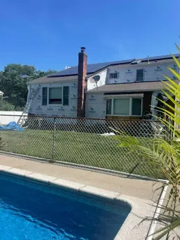 Backyard pool beside a house with a chain-link fence and blue sky