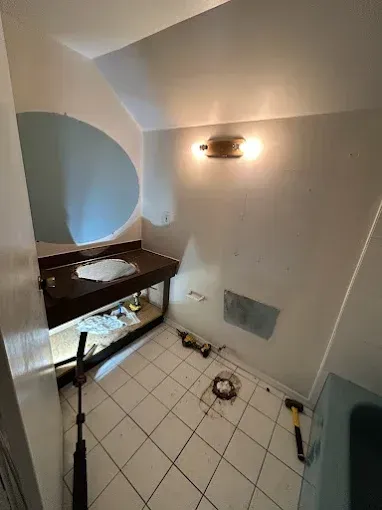 Bathroom with tiled floor, vanity mirror, wall light, and tools on the floor during renovation