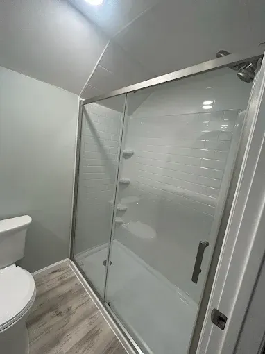 Modern bathroom with glass-enclosed shower and toilet, gray walls, and wood-look flooring