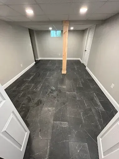 Empty finished basement room with gray walls, dark tiled floor, recessed lights, and a wooden support post.