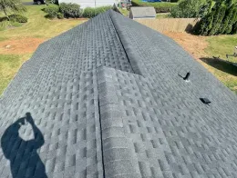 Roof shingles on a house, viewed from above with a shadow in the foreground and yard beyond