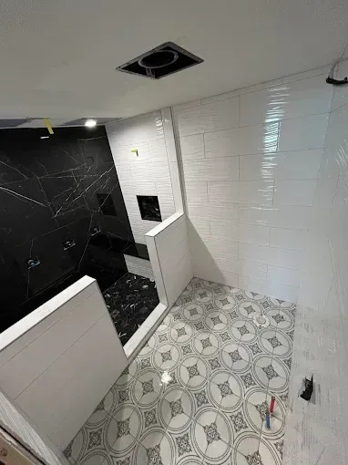 Partially tiled bathroom with black shower walls, white walls, and patterned floor tiles