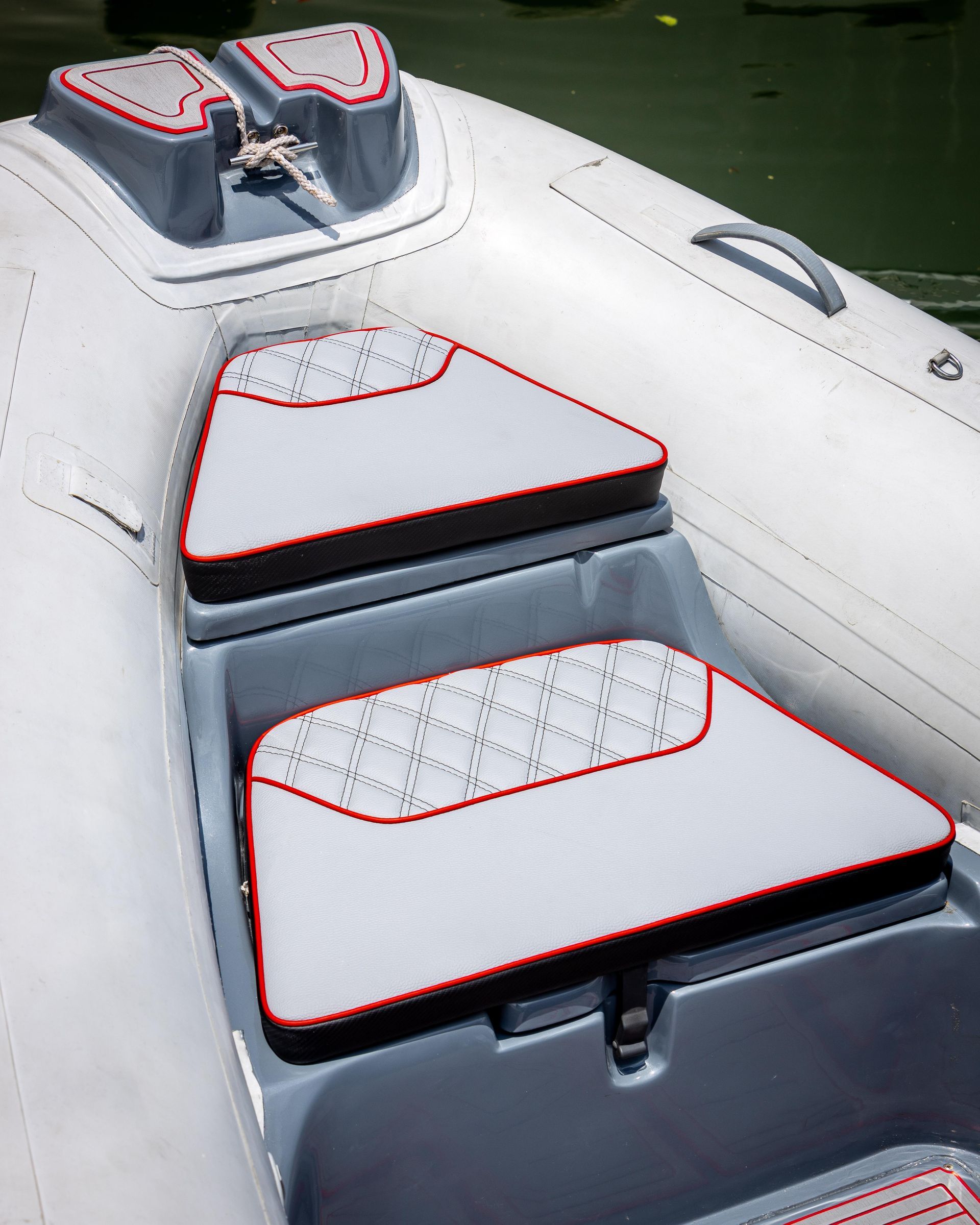 Two rows of beige and red upholstered boat seats under a black canopy, with a view of a hillside in the background.