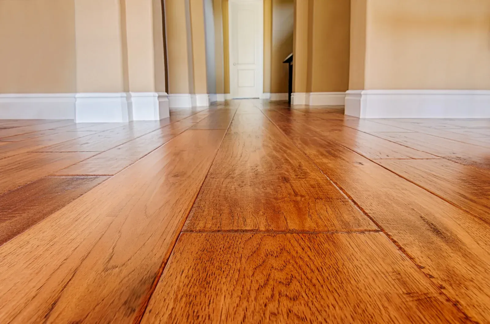 Low-angle view of glossy, natural-toned hardwood flooring extending through a doorway in a home.