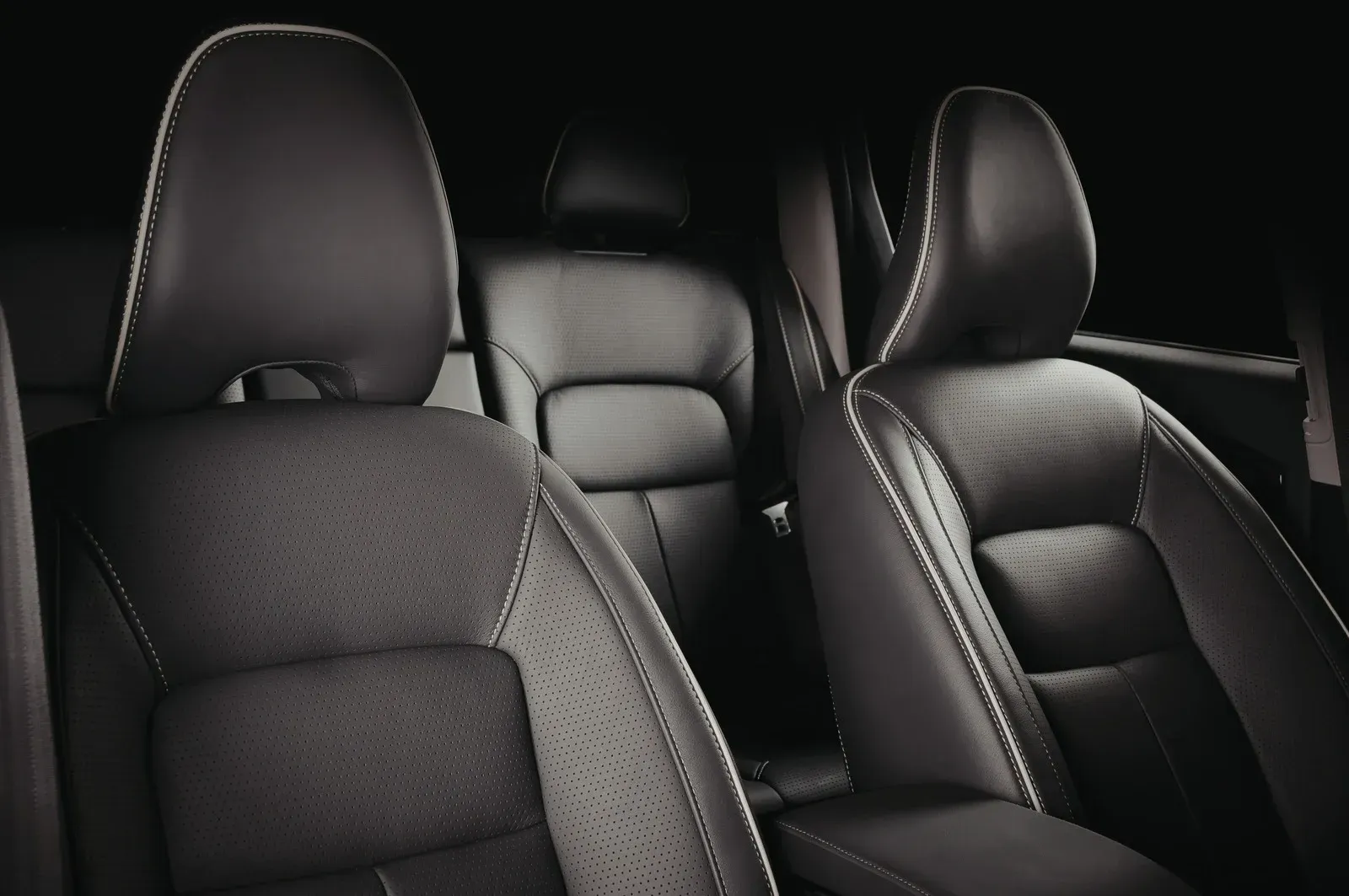 The interior of a vehicle featuring black leather front and rear seats with white stitching and perforated detailing.