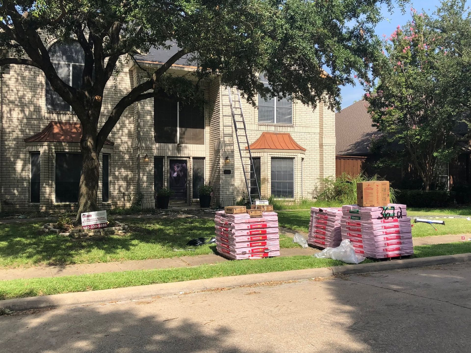 Stacks of bagged materials on a lawn in front of a stone house, with trees overhead.