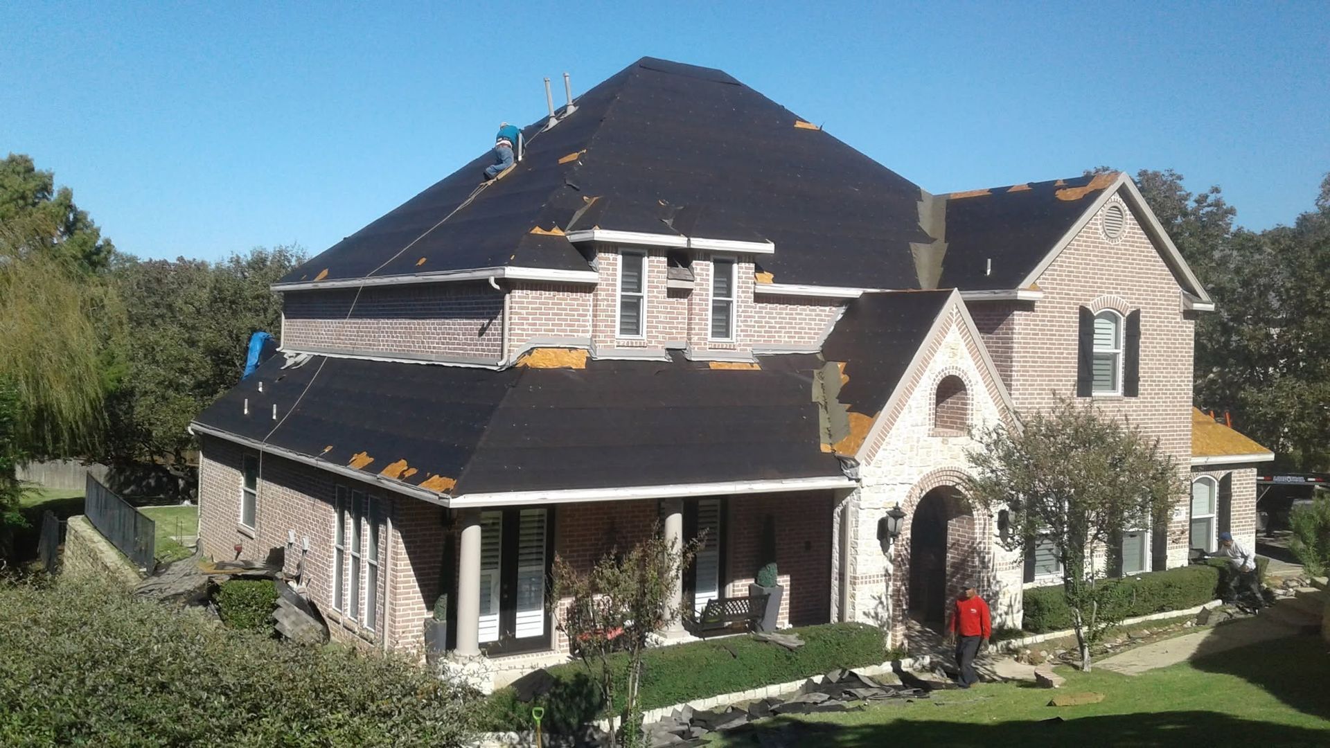 Large stone house with a dark roof, arched entry, and a person standing by the front door.