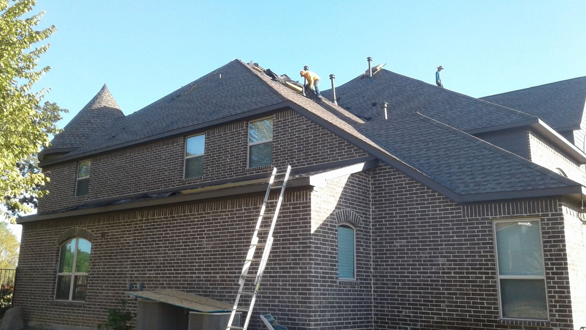 Brick house with a steep gray roof and a ladder leaning against the side