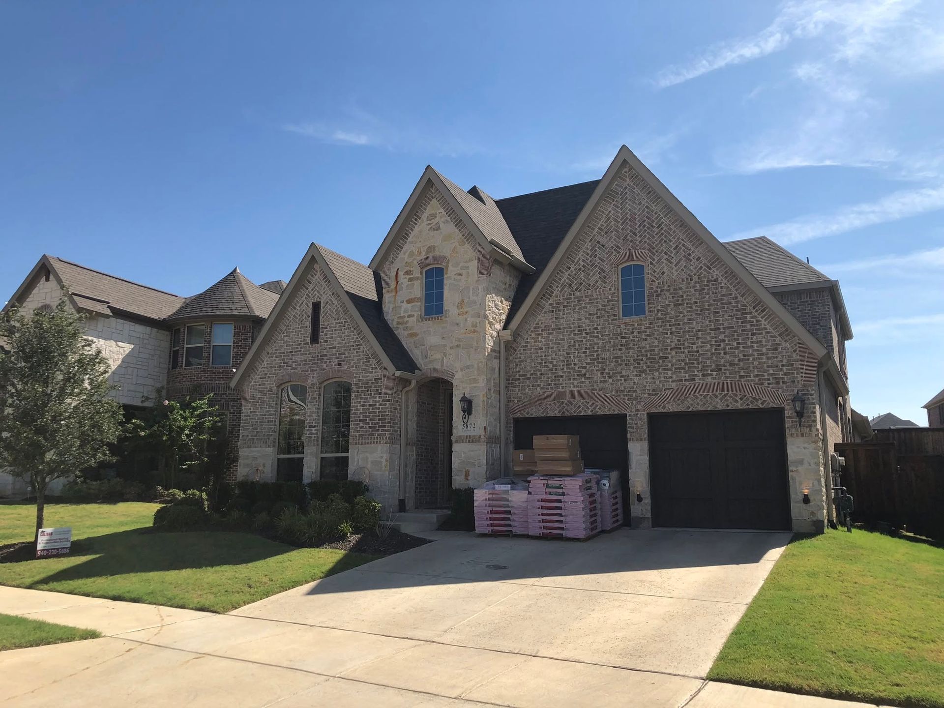 Stone suburban house with gabled roof, two-car garage, and a driveway under a blue sky