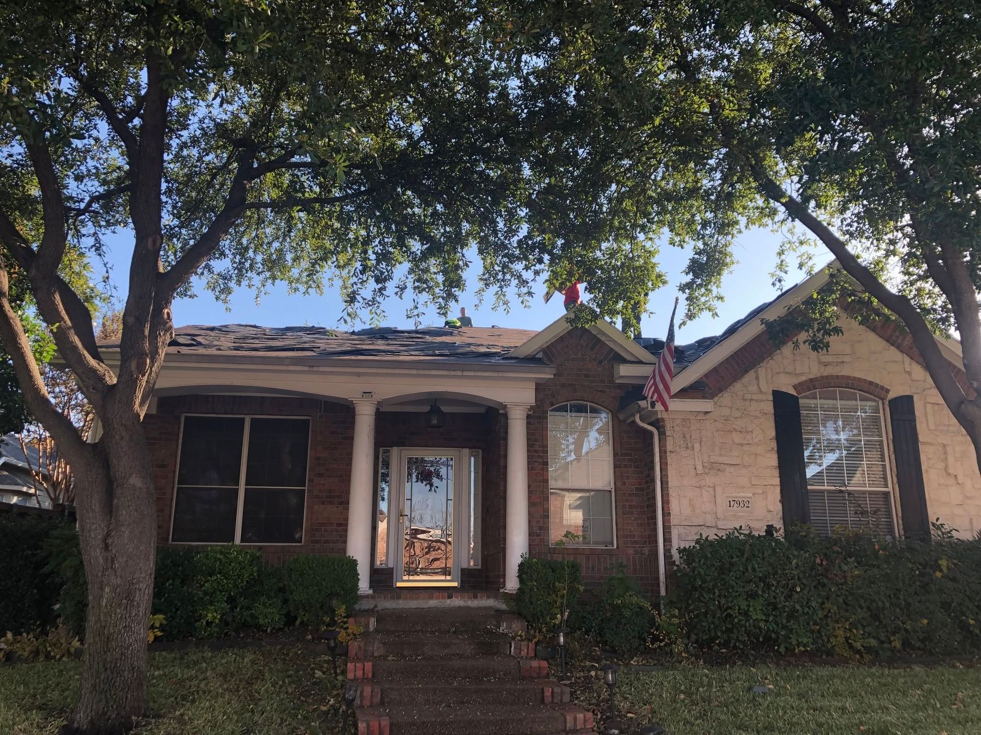 Single-story brick house with front steps, trees, and an American flag in the yard